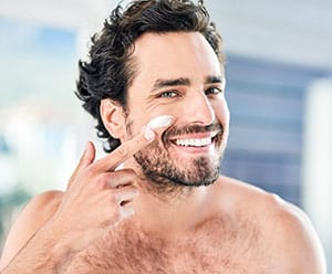 handsome young man applying moisturizer to his face