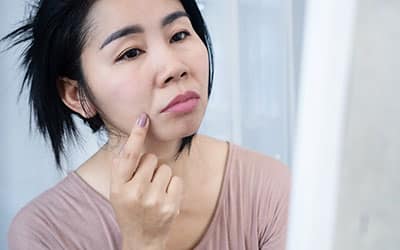 Asian woman worries about her face aging on a mirror with wrinkles skin nasolabial fold, smile lines, or laugh lines