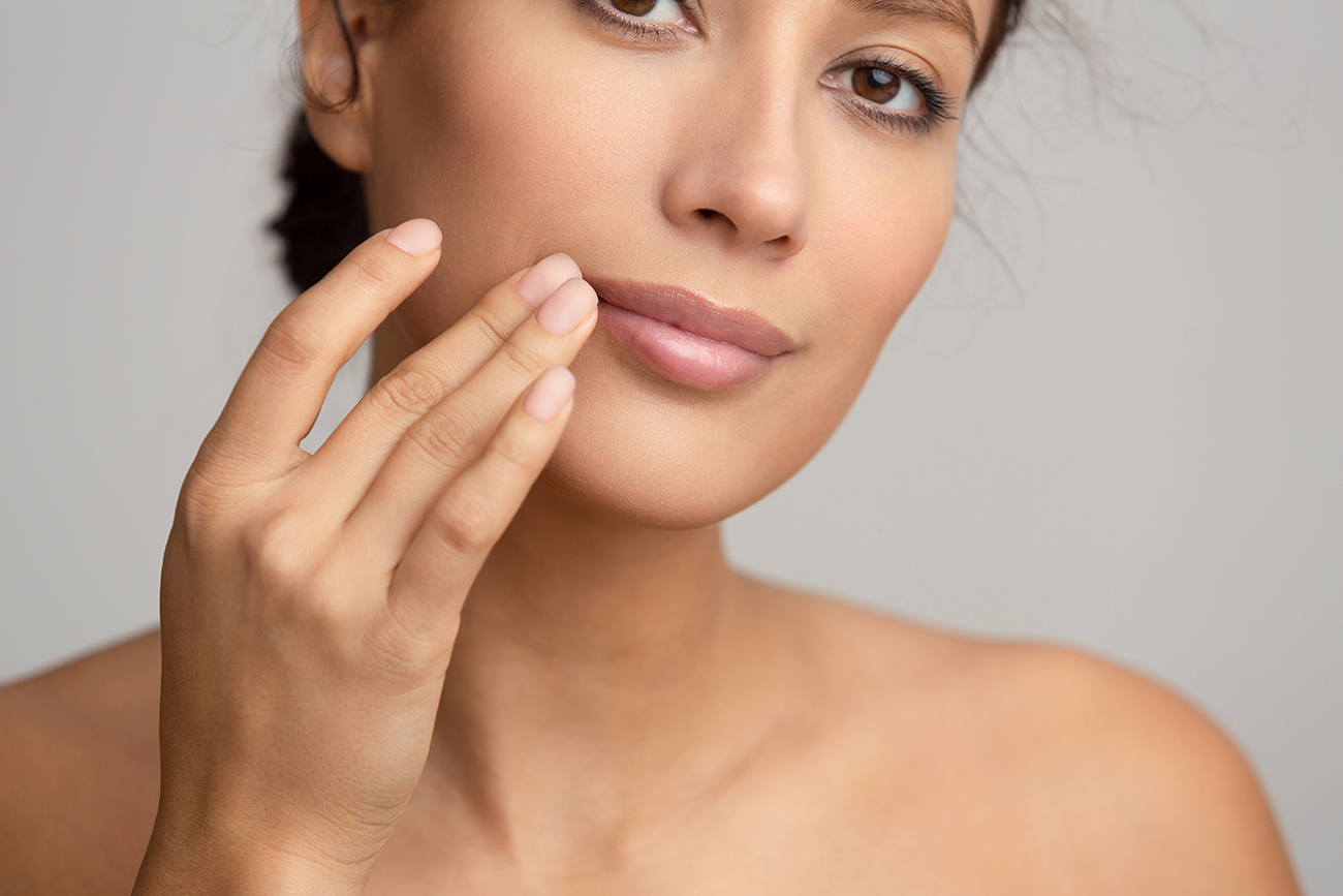 Woman applying skincare cream on her cheek with fingers, close-up face